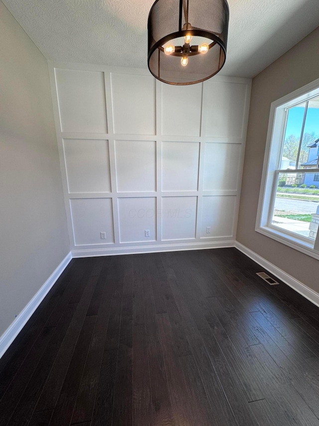 unfurnished dining area featuring dark wood-type flooring, visible vents, a textured ceiling, and baseboards
