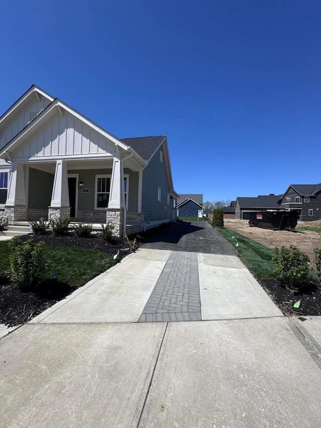 view of side of home with driveway, covered porch, board and batten siding, and stone siding
