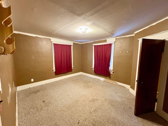 empty room with carpet, a textured ceiling, and baseboards