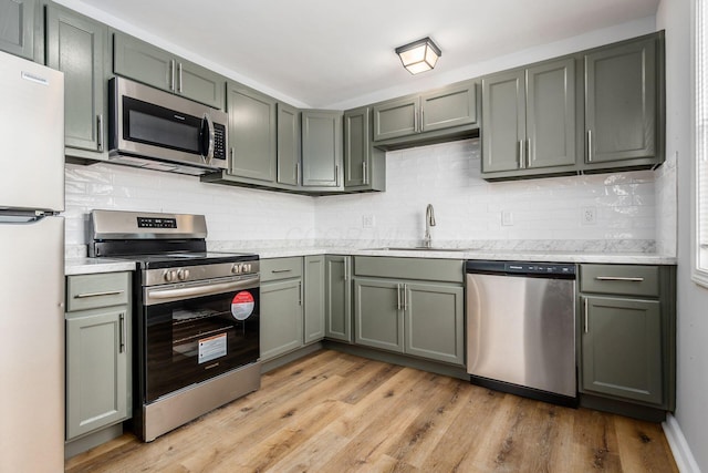 kitchen with light wood-style flooring, appliances with stainless steel finishes, a sink, light countertops, and backsplash