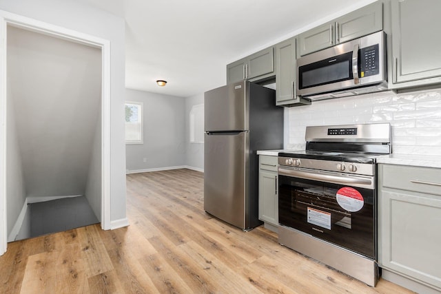 kitchen featuring tasteful backsplash, gray cabinets, stainless steel appliances, light countertops, and light wood-type flooring