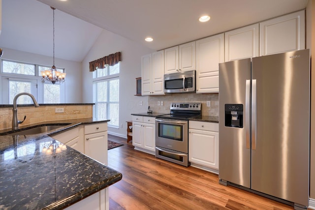 kitchen with white cabinetry, stainless steel appliances, sink, dark stone countertops, and pendant lighting