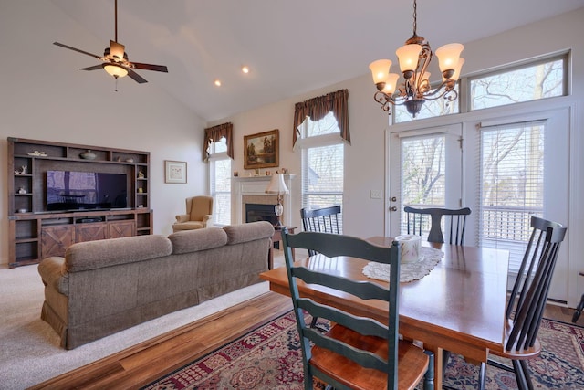 dining room with ceiling fan with notable chandelier, high vaulted ceiling, light hardwood / wood-style flooring, and a fireplace