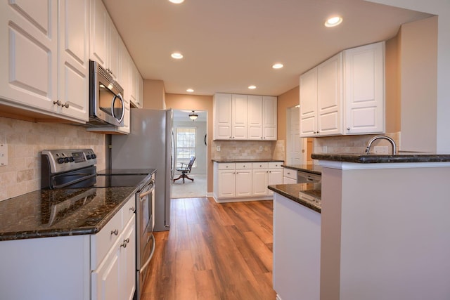 kitchen with light hardwood / wood-style flooring, stainless steel appliances, dark stone counters, decorative backsplash, and white cabinetry