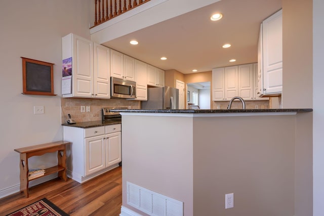 kitchen with appliances with stainless steel finishes, light hardwood / wood-style flooring, white cabinetry, and kitchen peninsula