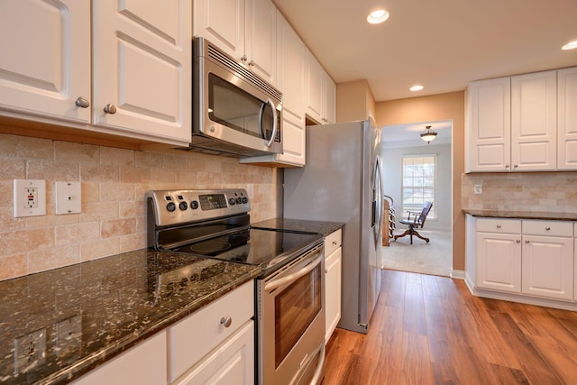 kitchen featuring light hardwood / wood-style flooring, stainless steel appliances, dark stone counters, decorative backsplash, and white cabinetry