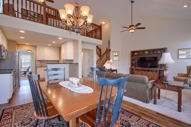 dining area with ceiling fan with notable chandelier, light hardwood / wood-style flooring, and a high ceiling