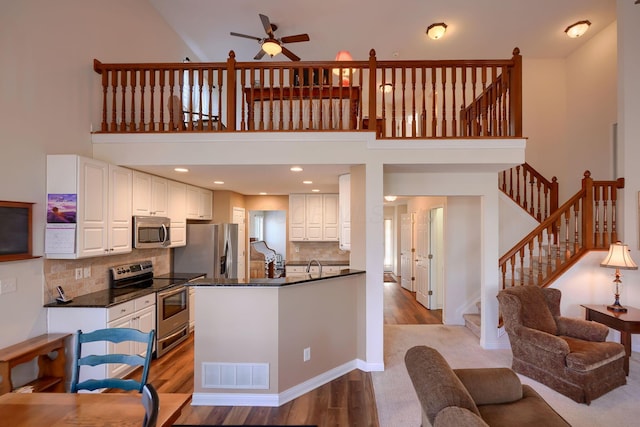 kitchen with white cabinets, a towering ceiling, stainless steel appliances, and light hardwood / wood-style flooring