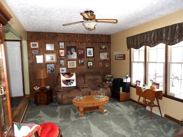 sitting room featuring ceiling fan, dark colored carpet, wood walls, and a textured ceiling