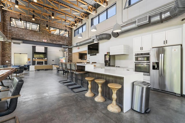 kitchen with a breakfast bar, a high ceiling, light countertops, white cabinetry, and appliances with stainless steel finishes