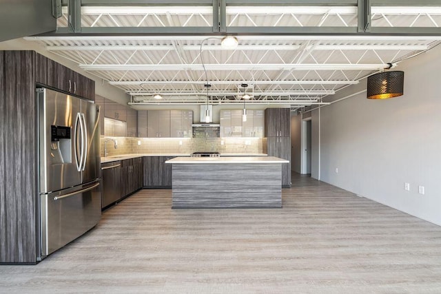 kitchen featuring wall chimney range hood, appliances with stainless steel finishes, modern cabinets, light wood-type flooring, and light countertops