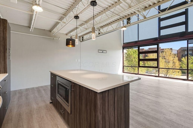 kitchen with light countertops, stainless steel microwave, dark brown cabinetry, and light wood finished floors