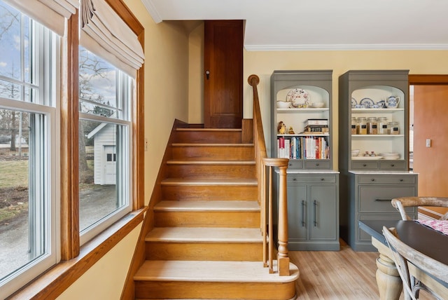 staircase with ornamental molding, a healthy amount of sunlight, and wood finished floors