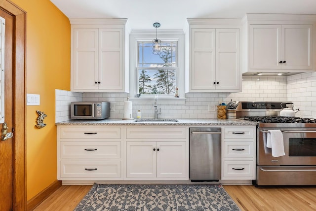 kitchen with appliances with stainless steel finishes, white cabinets, a sink, and light wood-style flooring