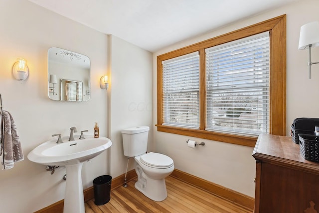 half bath with baseboards, toilet, and wood finished floors