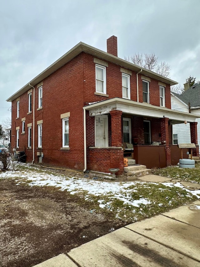 view of front of home featuring covered porch, brick siding, and a chimney