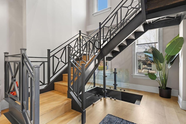 staircase featuring wood finished floors, baseboards, and a towering ceiling