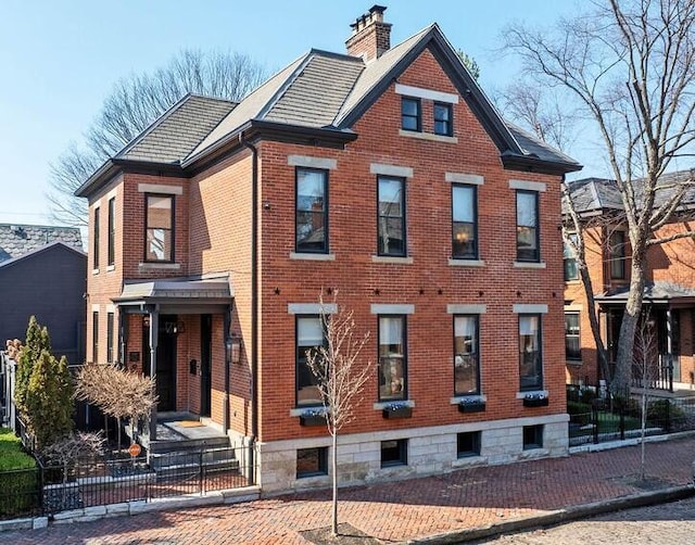 view of front of house featuring brick siding, a chimney, roof with shingles, and fence