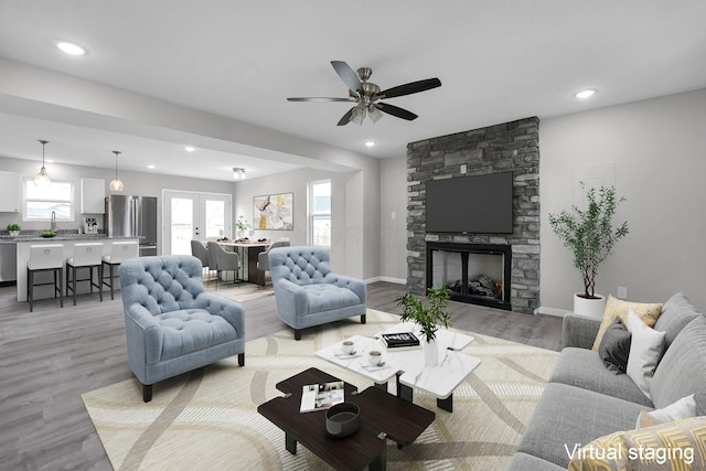 living room featuring recessed lighting, a stone fireplace, light wood-style flooring, and baseboards