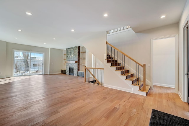 unfurnished living room featuring built in shelves, recessed lighting, a stone fireplace, light wood-type flooring, and baseboards