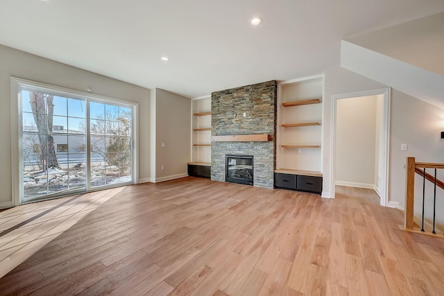 unfurnished living room featuring built in features, recessed lighting, light wood-style floors, a stone fireplace, and baseboards