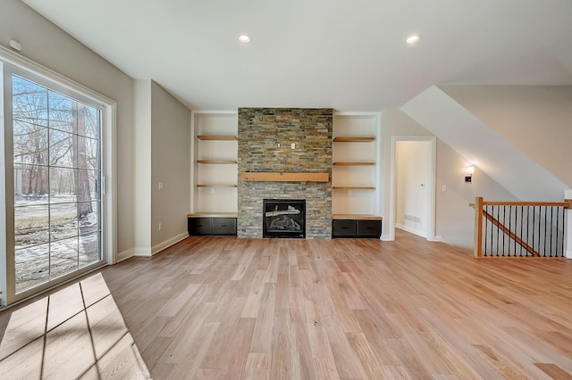 unfurnished living room with built in shelves, light wood-type flooring, and a stone fireplace