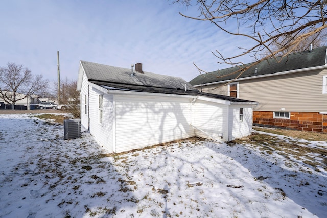 snow covered property with roof with shingles, a chimney, and central air condition unit