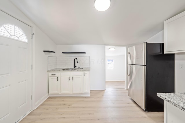 kitchen featuring light wood-style flooring, freestanding refrigerator, light stone countertops, white cabinetry, and a sink