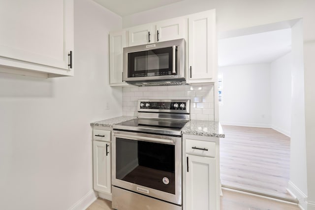 kitchen featuring light stone counters, stainless steel appliances, white cabinetry, baseboards, and decorative backsplash