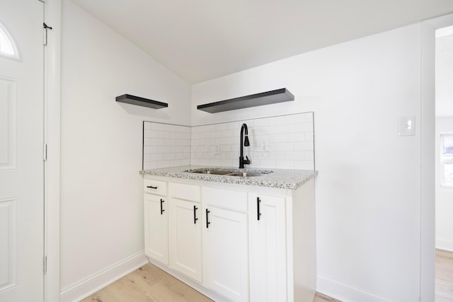 kitchen featuring light stone counters, a sink, light wood-style floors, white cabinets, and backsplash