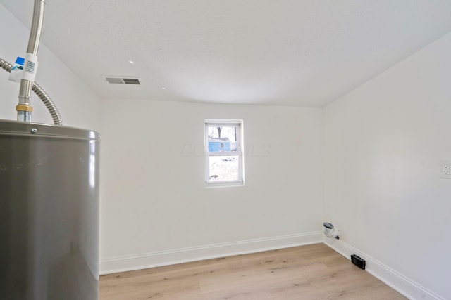 laundry area featuring light wood-type flooring, baseboards, water heater, and visible vents