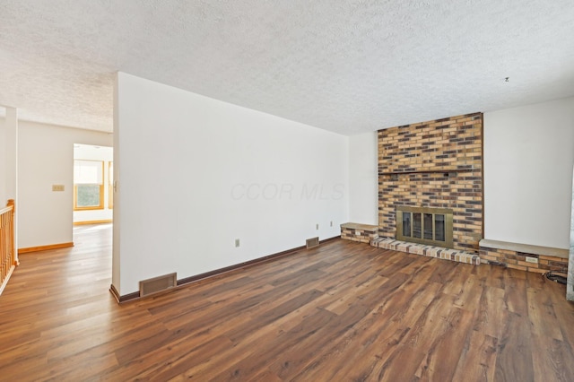 unfurnished living room featuring visible vents, a fireplace, a textured ceiling, and wood finished floors