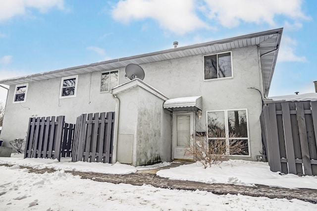 snow covered back of property featuring fence and stucco siding