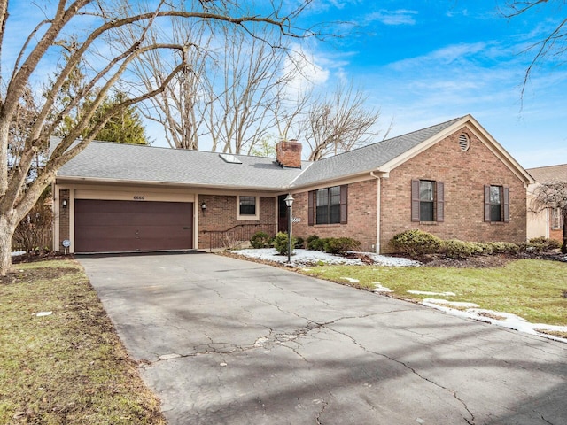 ranch-style home with brick siding, a chimney, an attached garage, driveway, and a front lawn