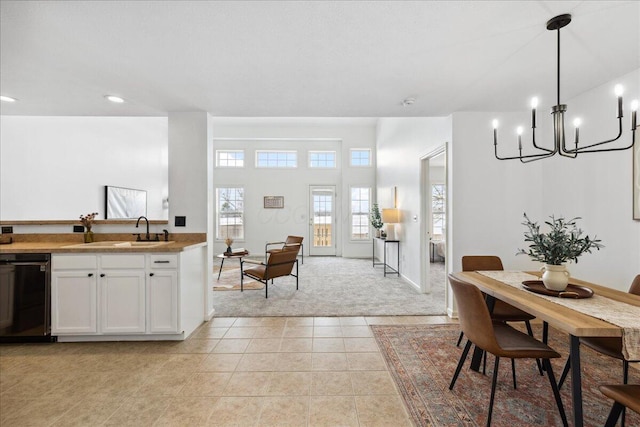 kitchen featuring light tile patterned floors, a sink, white cabinets, black dishwasher, and decorative light fixtures