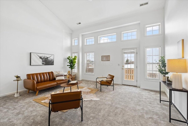 living area with a towering ceiling, a healthy amount of sunlight, visible vents, and light colored carpet