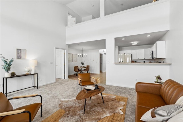 living room featuring a towering ceiling, baseboards, a chandelier, and light colored carpet