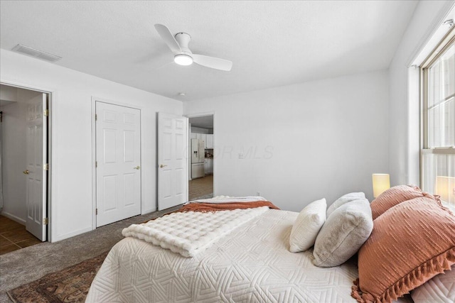 bedroom featuring white refrigerator with ice dispenser, visible vents, dark carpet, and a ceiling fan