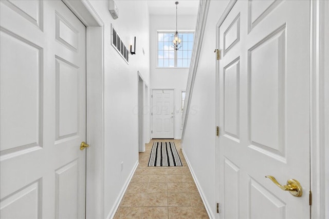 hallway with baseboards, visible vents, a towering ceiling, an inviting chandelier, and light tile patterned flooring