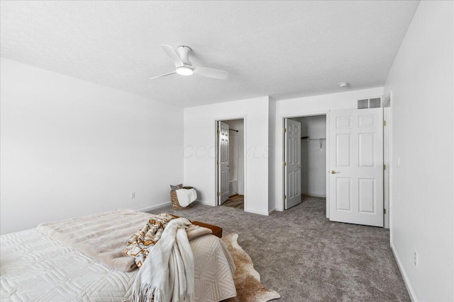 carpeted bedroom featuring a walk in closet, visible vents, a ceiling fan, a textured ceiling, and baseboards