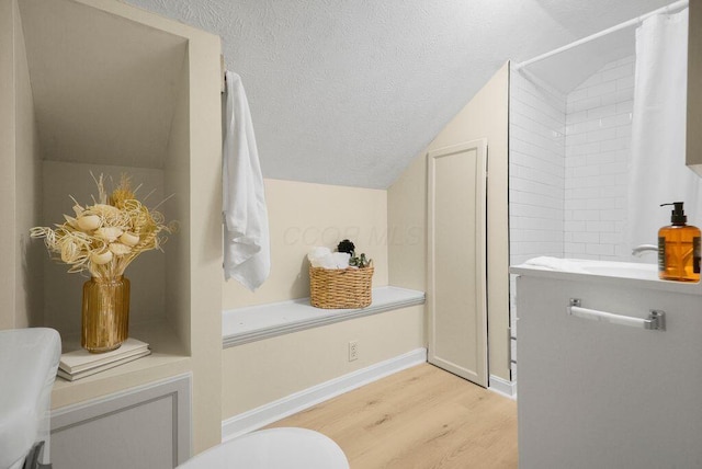 bathroom with a textured ceiling, toilet, vaulted ceiling, and wood-type flooring