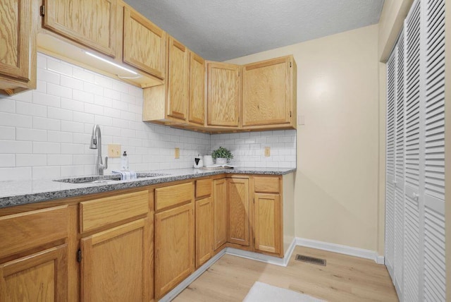 kitchen with light wood-type flooring, light stone countertops, sink, a textured ceiling, and decorative backsplash