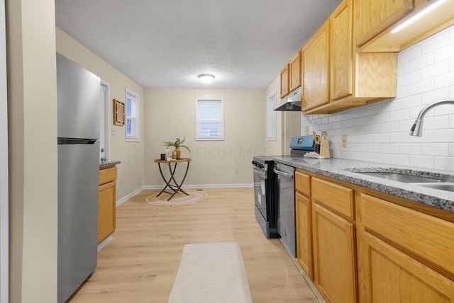 kitchen featuring appliances with stainless steel finishes, light hardwood / wood-style flooring, stone counters, backsplash, and sink