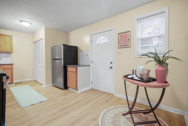 kitchen with stainless steel refrigerator, tasteful backsplash, light brown cabinets, and light hardwood / wood-style flooring