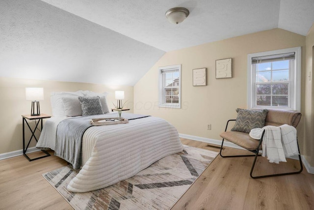 bedroom with light hardwood / wood-style floors, multiple windows, a textured ceiling, and lofted ceiling