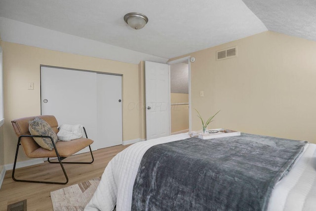 bedroom with light wood-type flooring, a closet, and vaulted ceiling