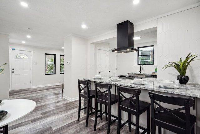 kitchen featuring wood-type flooring, a breakfast bar, light stone counters, island range hood, and a textured ceiling