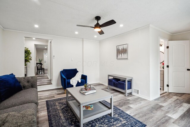 living room with light hardwood / wood-style floors, a textured ceiling, ceiling fan, and ornamental molding