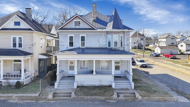 view of front of property featuring covered porch, a residential view, and a standing seam roof