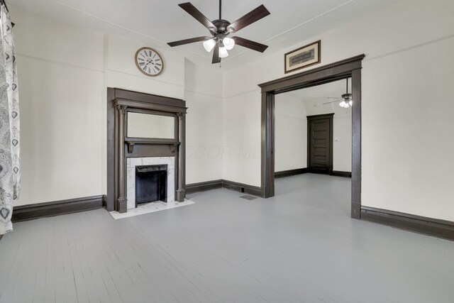 unfurnished living room with ceiling fan, a premium fireplace, and baseboards